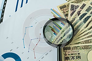 Magnifying glass on pile of japanese yen banknotes with printed