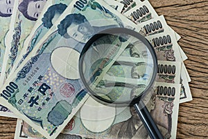 Magnifying glass on pile of japanese yen banknotes on wooden tab