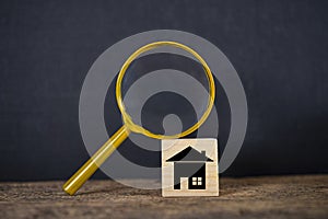 A magnifying glass is placed on a wooden block. House is on a wooden block