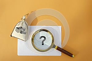 Magnifying glass with a question mark and a money bag. Business and finance concept. The question of investment. Financial