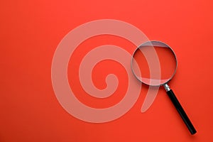 Magnifying glass on red background, top view. Space for text