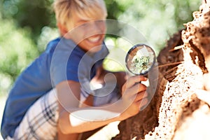 Magnifying glass, search and nature with curious boy outdoor in park, garden or field for discovery. Kids, learning and
