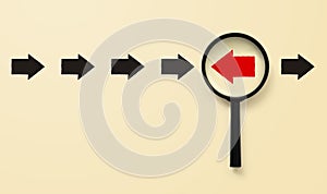 Magnifying glass searching for red arrow facing the opposite direction black arrows