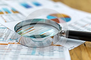 A magnifying glass sits atop a piece of paper, magnifying the text and details on the page, A magnifying glass over financial
