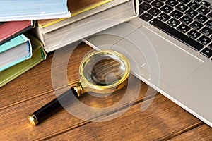 Magnifying glass and a stack of books on the laptop keyboard. The concept of information search on the Internet and books