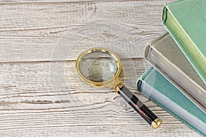 A magnifying glass and a stack of books on a wooden table. The concept of getting knowledge from books. Selective focus