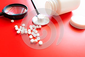 Magnifying glass, tablets and bottle on red reflection background. Checking ingredients and effectiveness of medicine