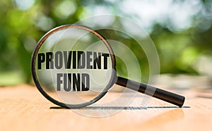 Magnifying glass with text PROVIDENT FUND on wooden table and green background