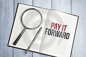 magnifying glass and a white notebook with the text we PAY IT FORWARD