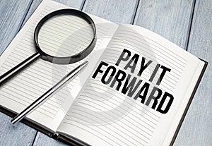 magnifying glass and a white notebook with the text we PAY IT FORWARD