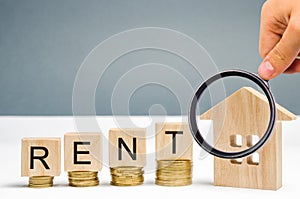 Magnifying glass, wooden blocks with the word Rent, coins and a miniature house. The concept of renting housing and real estate.