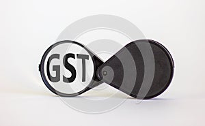 Magnifying glass with word GST - goods and services tax - on beautiful white background. Business concept, copy space