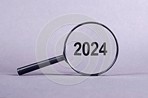 Magnifying glass with word numbers 2024 on gray background. Focused on business concept. Search new idea