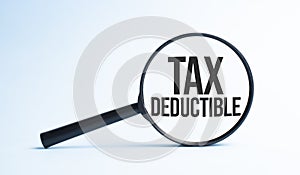 Magnifying glass with the word TAX DEDUCTIBLE. Business concept