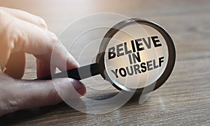 Magnifying glassand phrase Believe in yourself on wooden table. Motivation concept