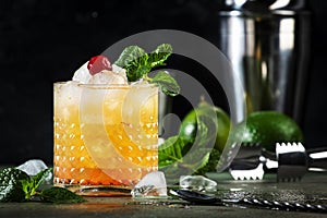 Mai Tai trendy alcoholic cocktail with rum, liqueur, syrup, lime juice, mint and crushed ice. Dark background, bar tools, copy