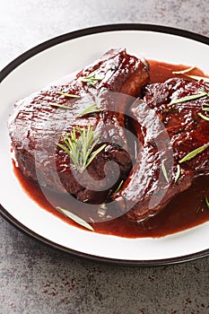 Maiale Ubriaco Drunken Pork chops in red wine sauce with herbs closeup on the plate. Vertical photo