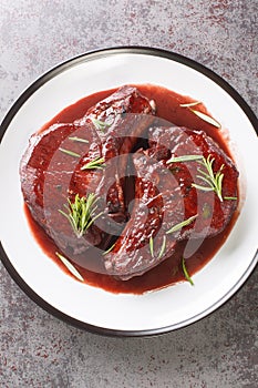 Maiale Ubriaco Drunken Pork chops in red wine sauce with herbs closeup on the plate. Vertical top view photo