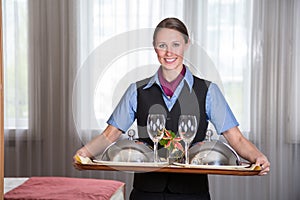 Maid in a hotel posing with tray in bedroom