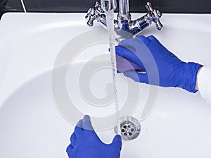 Maid or housewife cleaning wash basin. Womanâ€™s gloved hands washing white washbasin. Cleaning service concept at home 