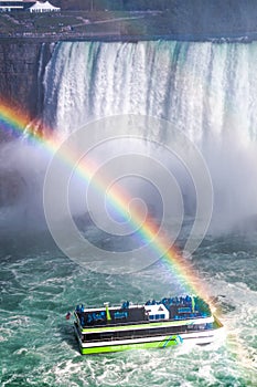 Maid of the Mist passing below a waterfall with a rainbow above it - Niagara Falls, Ontario