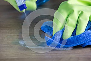 Maid with rubber gloves cleaning the table with a microfiber cloth and sterilizing spray bottle