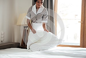 Maid setting up white bed sheet in hotel room