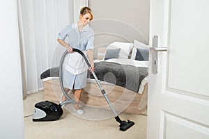 Maid with vacuum cleaner in hotel room photo