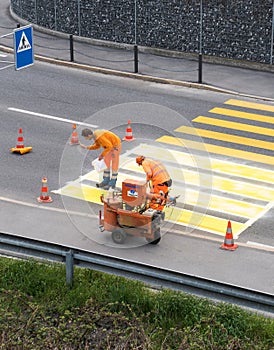 Maienfeld, GR / Switzerland - April 2, 2019: workers painting and marking a pedestrian crosswalk with fresh yellow paint to ensure