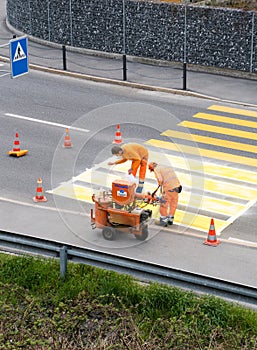 Maienfeld, GR / Switzerland - April 2, 2019: workers painting and marking a pedestrian crosswalk with fresh yellow paint to ensure