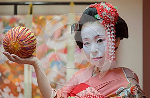 Maiko in kimono holding a temari ball in the hand.