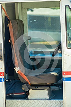Mail delivery truck with red and blue stipes on white van with brown seat and visible seatbelt to deliver mail to