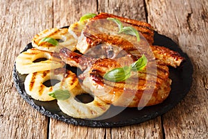 Main course: grilled pork chop steak in honey glaze with pineapples close-up on a slate plate. horizontal