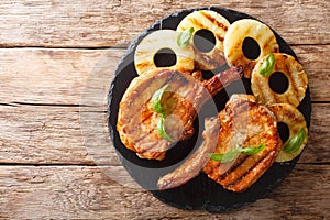 Main course: grilled pork chop steak in honey glaze with pineapples close-up on a slate plate. horizontal top view