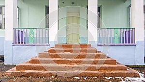 The main entrance to the building. Concrete brown staircase. Multi-colored wooden fence