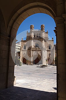 Main square of Castellon de la Plana through an arch with the Co-Cathedral of Santa Maria in the background on a sunny day with a photo