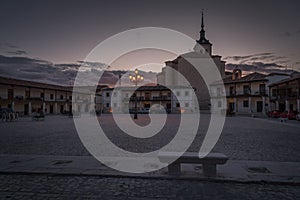 The main square of a Colmenar de Oreja surrounded by the stone houses at sunset with a stone bench in the foreground, Madrid, photo