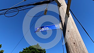 Main Street sign on old wooden electrical pole under blue sky, pan left.