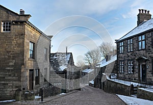 Main street in the village of Heptonstall in west Yorkshire with snow on roofs with blue winter sky