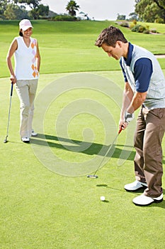 Maintaining careful focus on the green. Young couple playing golf together on the green.