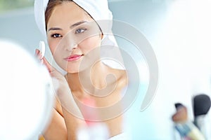 Maintaining her flawless beauty. An attactive young Asian woman applying moisturizer with a towel on her head.