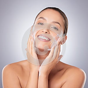 Maintaining my soft skin. a young beautiful woman washing her face against a grey background.