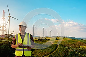 Maintenance engineer holding a tablet while working on wind turbine farm and thinking about saving energy design and possibility