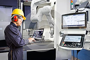 Maintenance engineer using laptop computer control automatic robotic hand with CNC machine in smart factory, Industry 4.0 concept