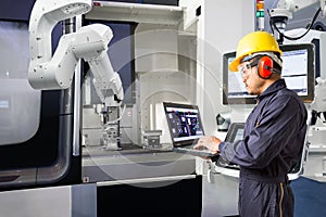 Maintenance engineer using laptop computer control automatic robotic hand with CNC machine in smart factory, Industry 4.0 concept