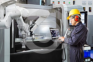 Maintenance engineer using laptop computer control automatic robotic hand with CNC machine in smart factory. Industry 4.0 concept