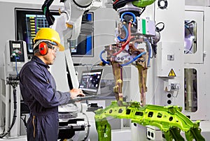 Maintenance engineer using laptop computer control robot grip automotive workpiece in smart factory, Industry 4.0 concept