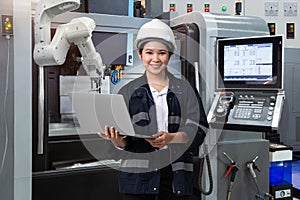 Maintenance female engineer using laptop computer control automatic robotic hand with CNC machine in smart factory, Industry 4.0