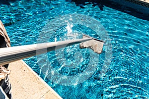 Maintenance man using a pool net leaf skimmer rake in summer to leave ready for bathing his pool