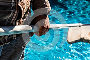 Maintenance man using a pool net leaf skimmer rake in summer to leave ready for bathing his pool